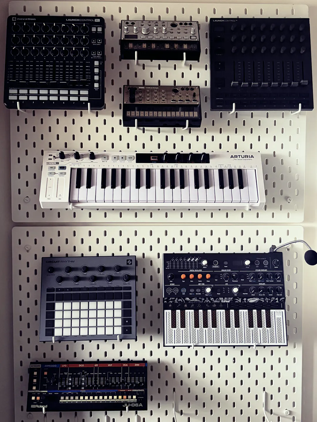 Novation, Korg, Arturia and Roland synths and controllers on a pegboard wall